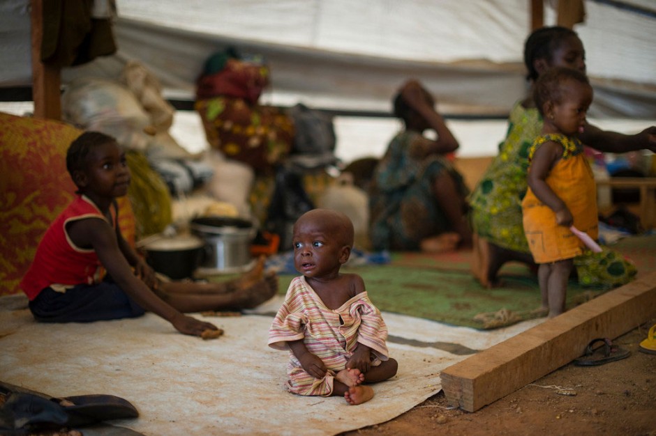 Menino de um ano de idade, que sofre de subnutrição, sentado debaixo de uma tenda onde ele e a sua família se abrigam, no Centro de Dom Bosco, em Bangui. Foto: OCHA/Phil Moore