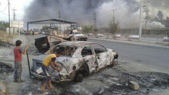 Crianças observam carro destruído após ofensiva terrorista em Mosul, no Iraque (Reuters)